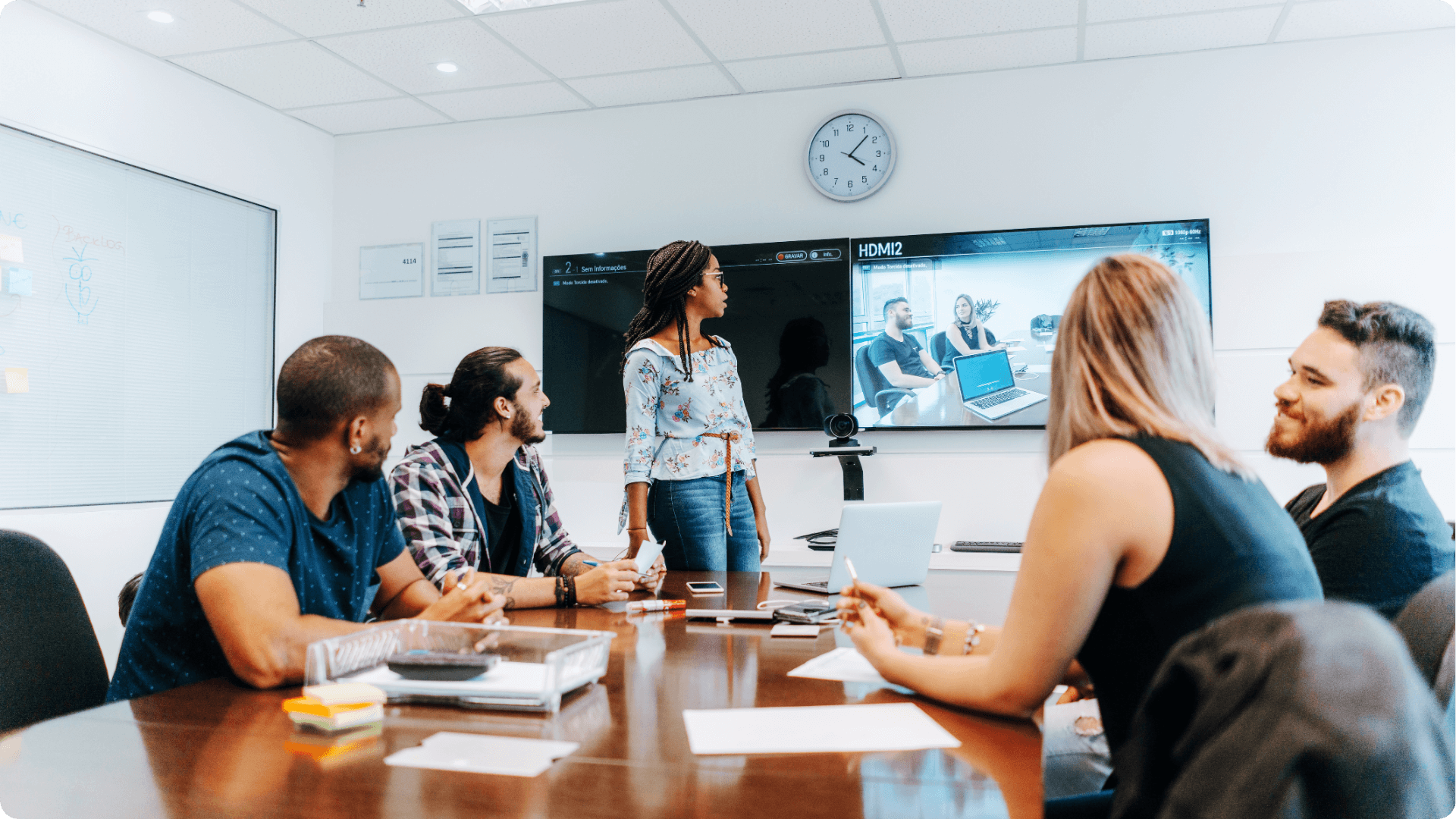 A group of It workers in an office around a desk having a video conference with people far away (1)