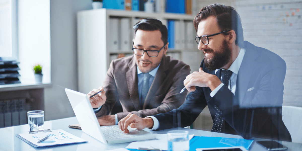 Two IT consultants executing BTPs advance services for a client at a table with a computer. (1)