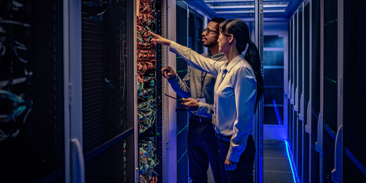 Two IT workers in a server room, checking out wiring on a large server. (1)