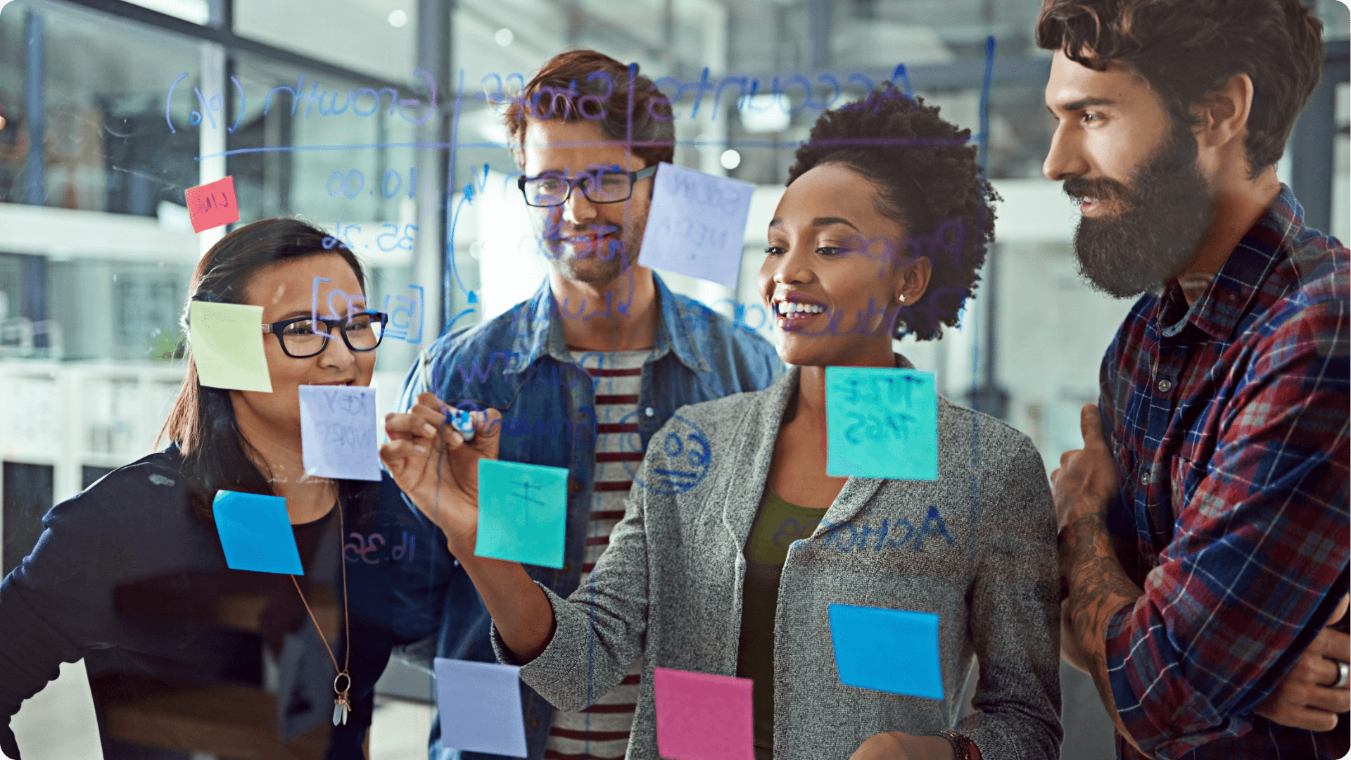 A group of tech workers using a glass board with sticky notes to come up with strategy. (1)