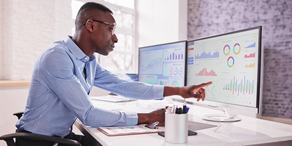 An IT worker pointing to data on a computer screen, while working on a computer with multiple monitors (1)
